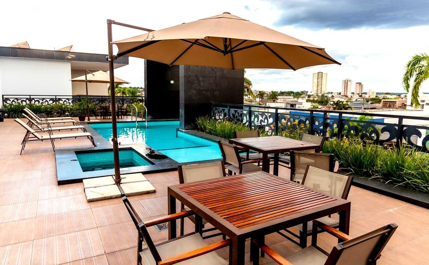 Área de piscina na cobertura de hotel com espreguiçadeiras, mesas de madeira e guarda-sol, com vista para a cidade